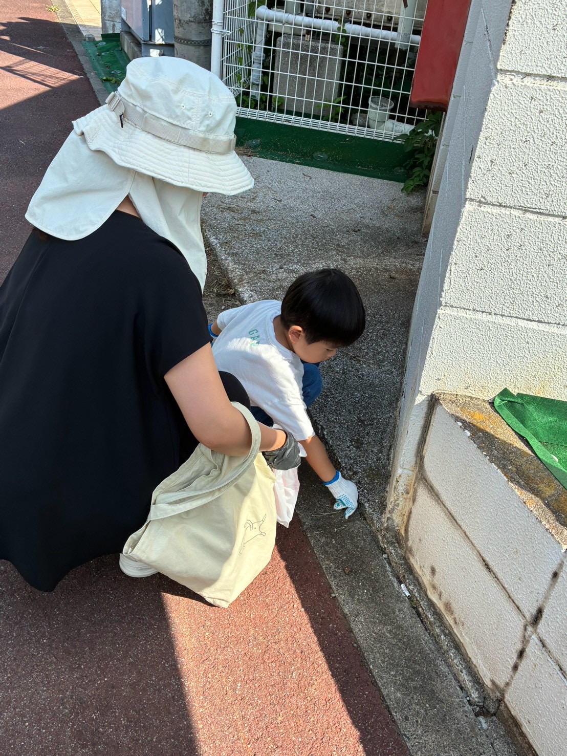 大人と子どもが一緒に壁際の小さなゴミを拾っている様子